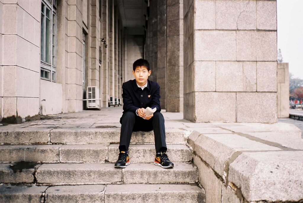 A young boy in school uniform and sneakers sits on the staircase of Pyongyang's National Library in North Korea