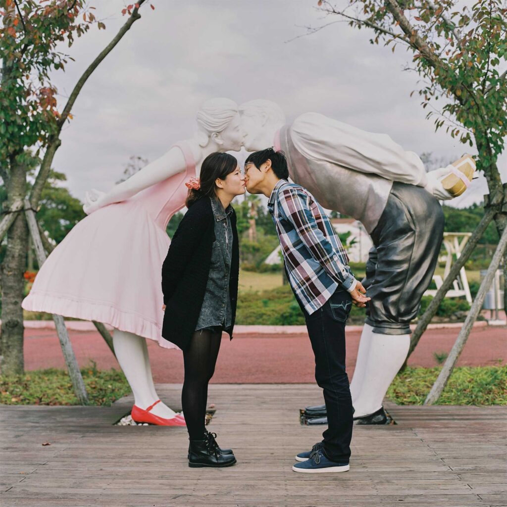 A young couple imitating the pose and kissing action of a sculpture depicting a female-male couple in Loveland sculpture park, Jejudo Island, South Korea