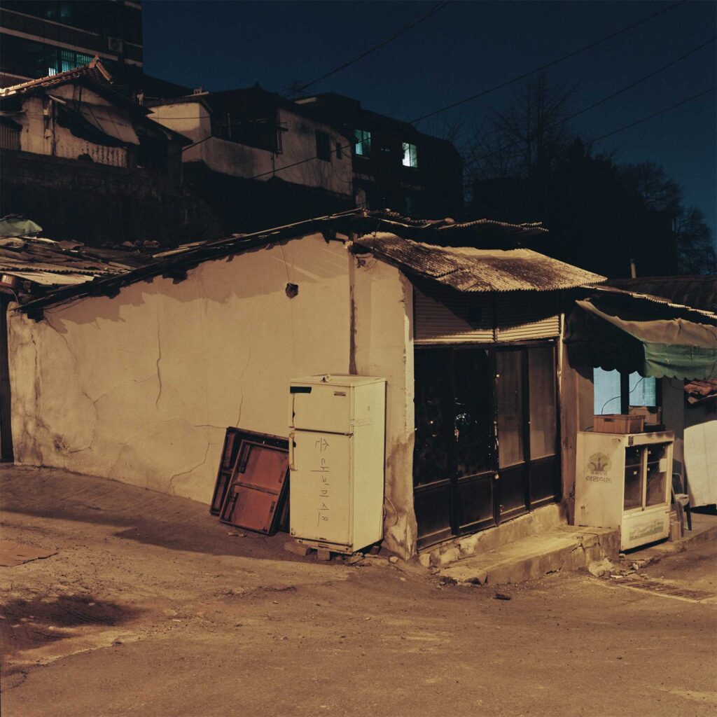 Night view of a small street corner building in an old Seoul neighborhood, facing construction