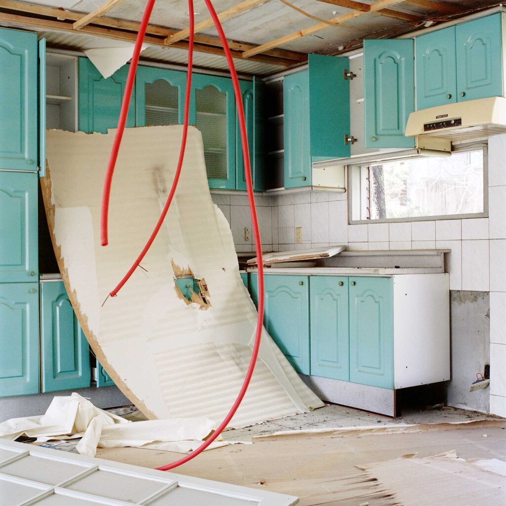 A mint-colored kitchen in an urban redevelopment area in Seoul, South Korea. The partially demolished ceiling reveals dangling red pipes reaching towards the kitchen floor