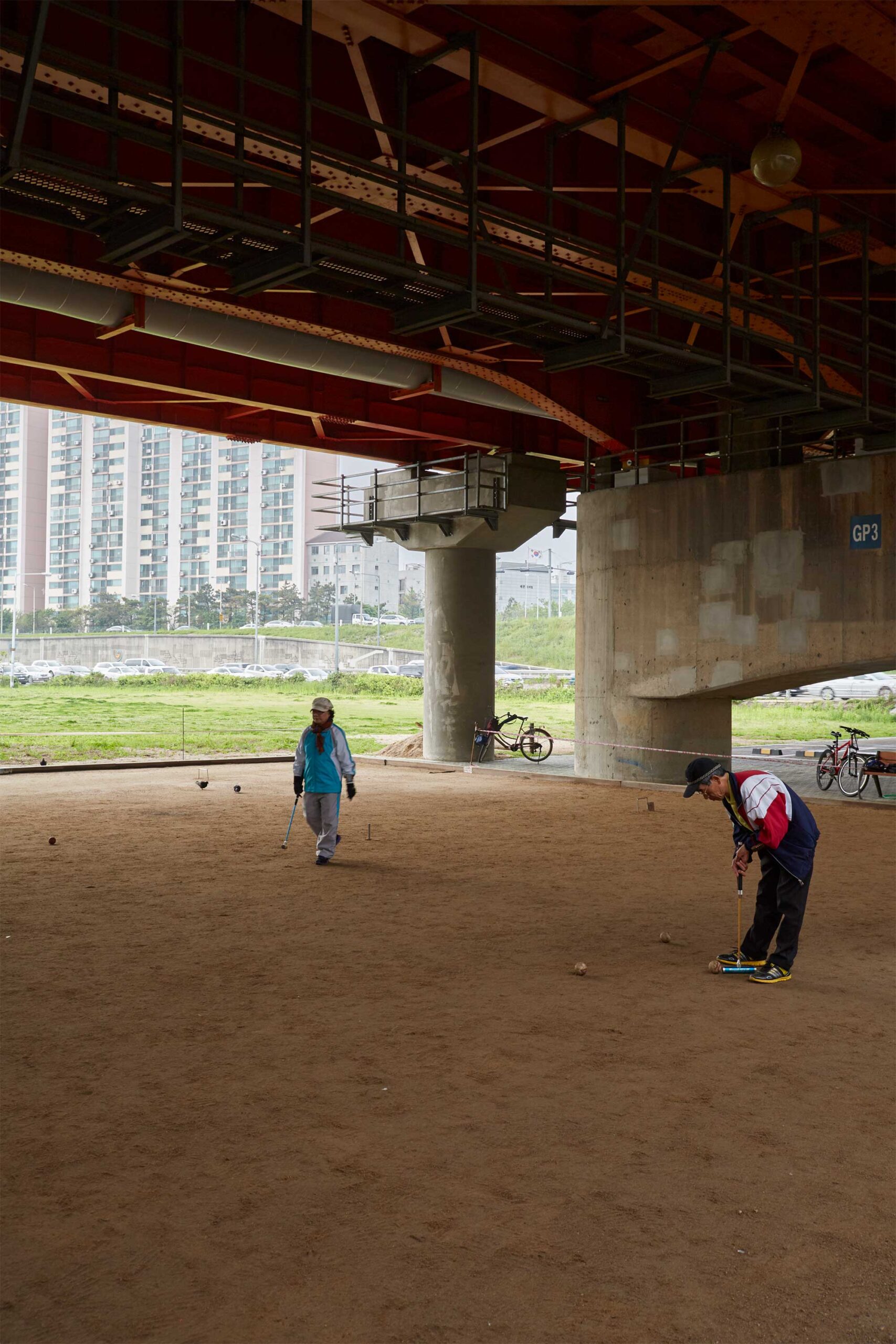 Two elderly people enjoy a game of croquet under a bridge spanning the Han River in Seoul, South Korea