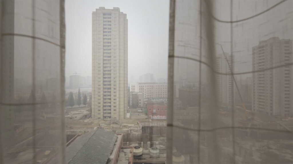 High-rise apartment complex seen through half-open curtain from hotel room, Pyongyang, North Korea