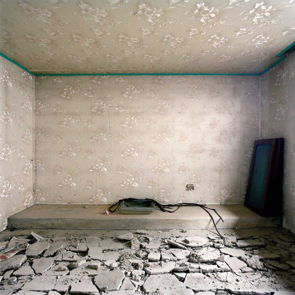 Beige flower-patterned wallpaper in an urban redevelopment area in Seoul, South Korea. A removed lamp sits on an elevated platform. The foreground: demolished concrete flooring