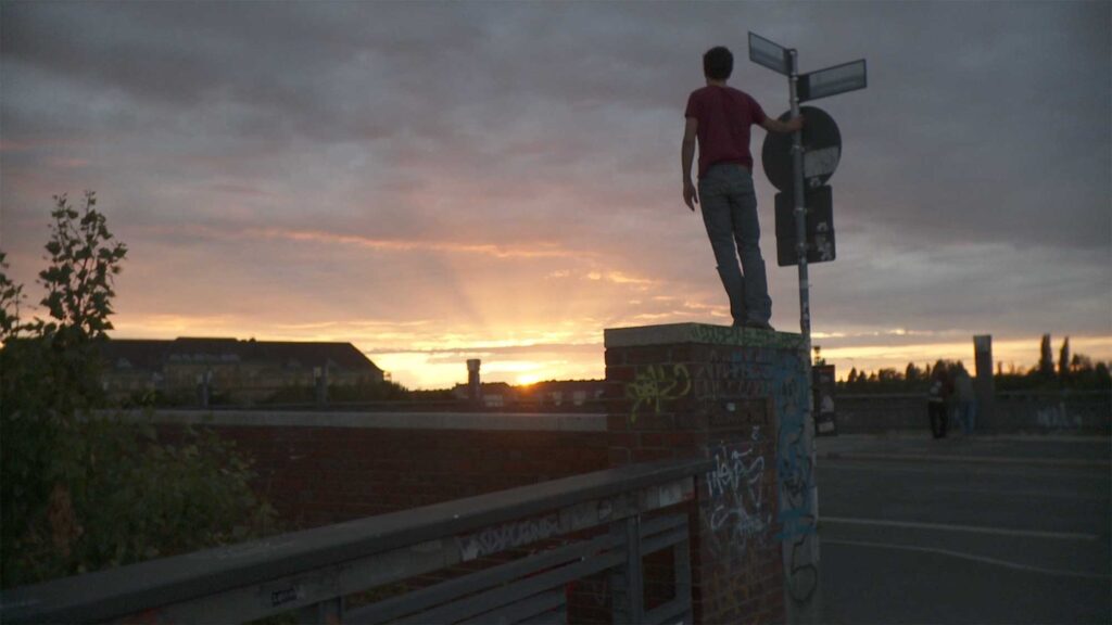 Crisjan Zollner stands on wall on street corner in Berlin as he looks at sunset
