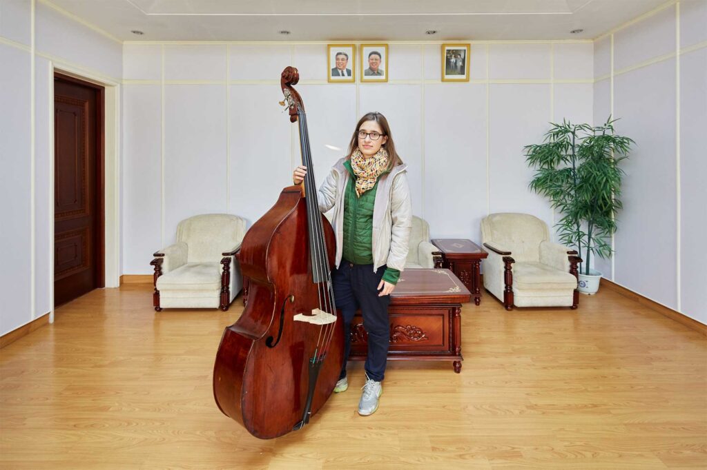 Munich Chamber Orchestra string bass player in Pyongyang, North Korea, with portraits of North Korean leaders Kim Il-Sung and Kim Jong-Il on the wall