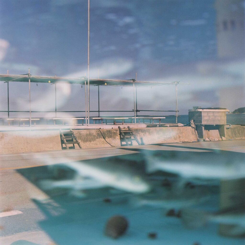 The reflection on a fish tank reveals a coastal road walled off from the ocean somewhere on the Korean East Coast