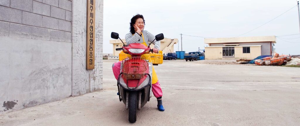 A portrait of a Haenyeo diver woman resting on her motorcycle on Jeju Island, South Korea