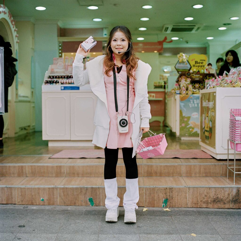 A young Korean lady stands in front of a cosmetics store in Seoul, South Korea, holding a microphone and cosmetic samples to attract passersby