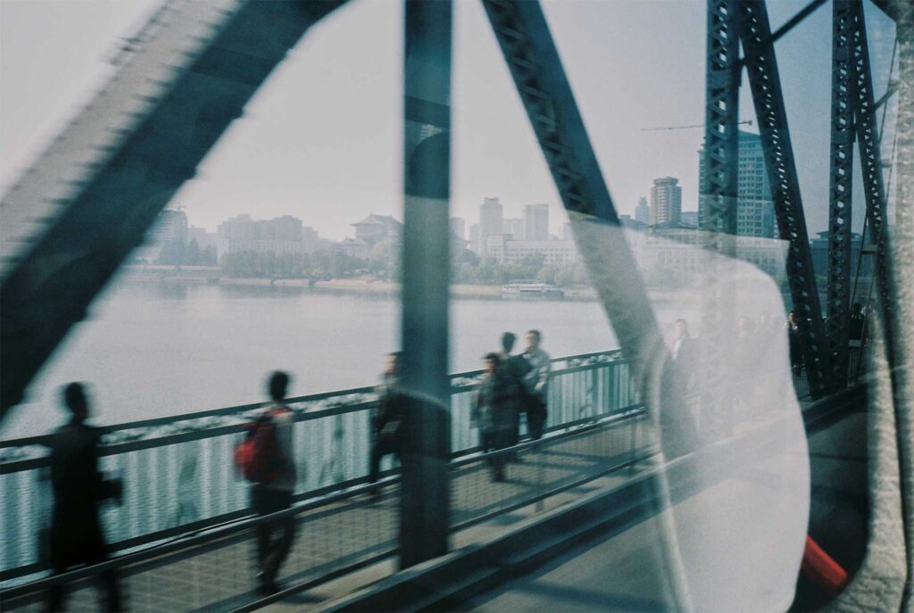 A snapshot from inside a bus captures pedestrians crossing the Taedong River bridge in Pyongyang, North Korea