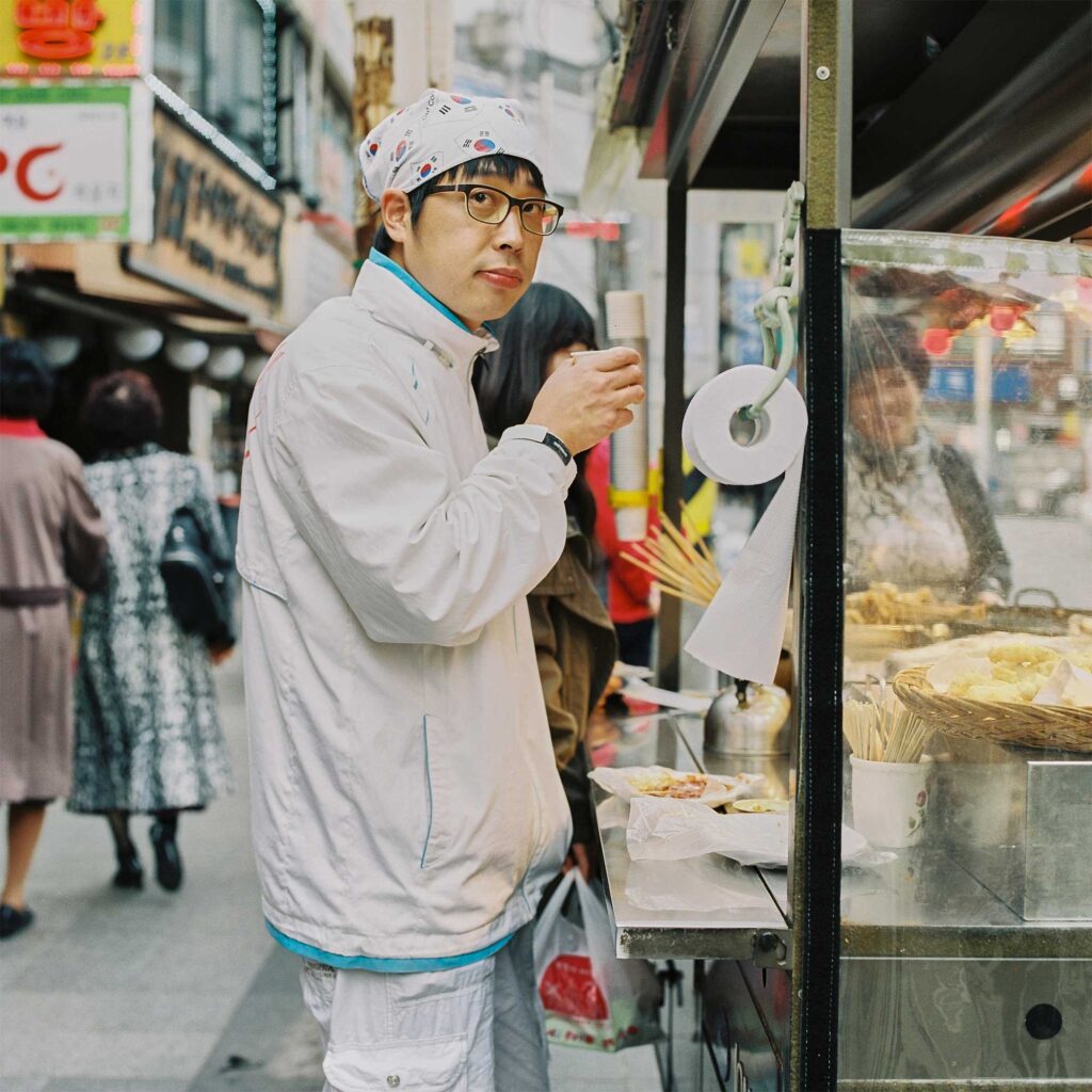 A young Korean man at a food stall in Seoul, South Korea, wearing a head cloth with printed Korean flags