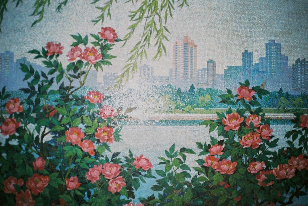 A mural at a subway station in Pyongyang, North Korea, depicts the cityscape with the Taedong River in the foreground, blossoming flowers along the riverbank, and towering apartment buildings in the background