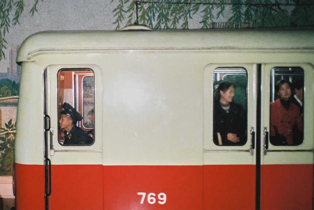A subway train pulling out of the station in Pyongyang, North Korea, with the driver and some passengers visible inside