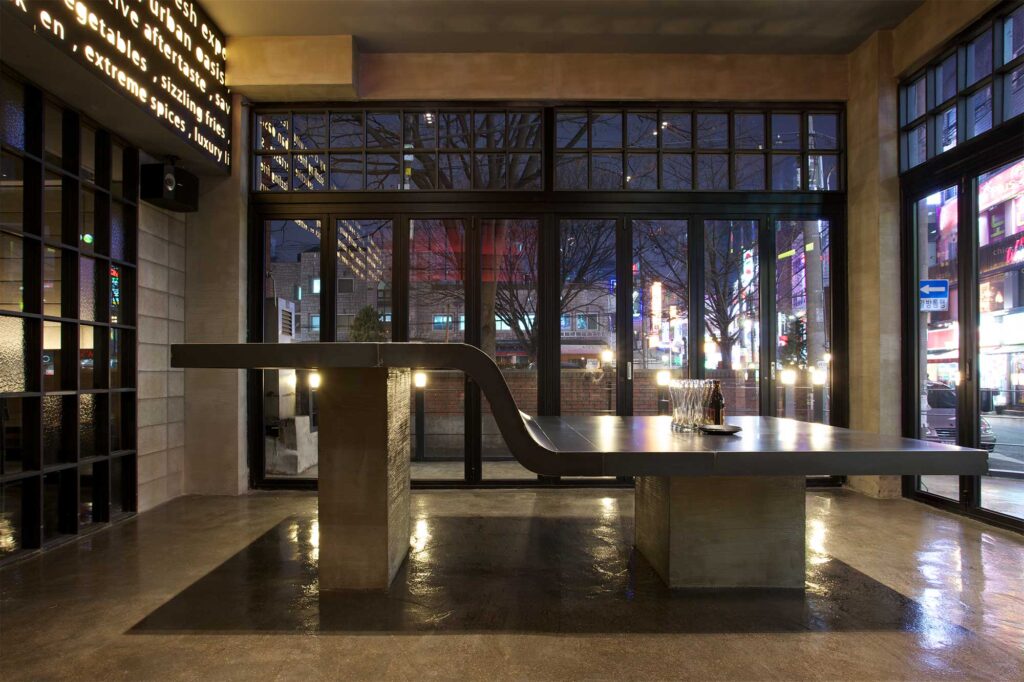 S-shaped standing and sitting counter area of Warehouse bar and restaurant in Seoul, South Korea, showcasing modern design with minimal decor using concrete and metal.