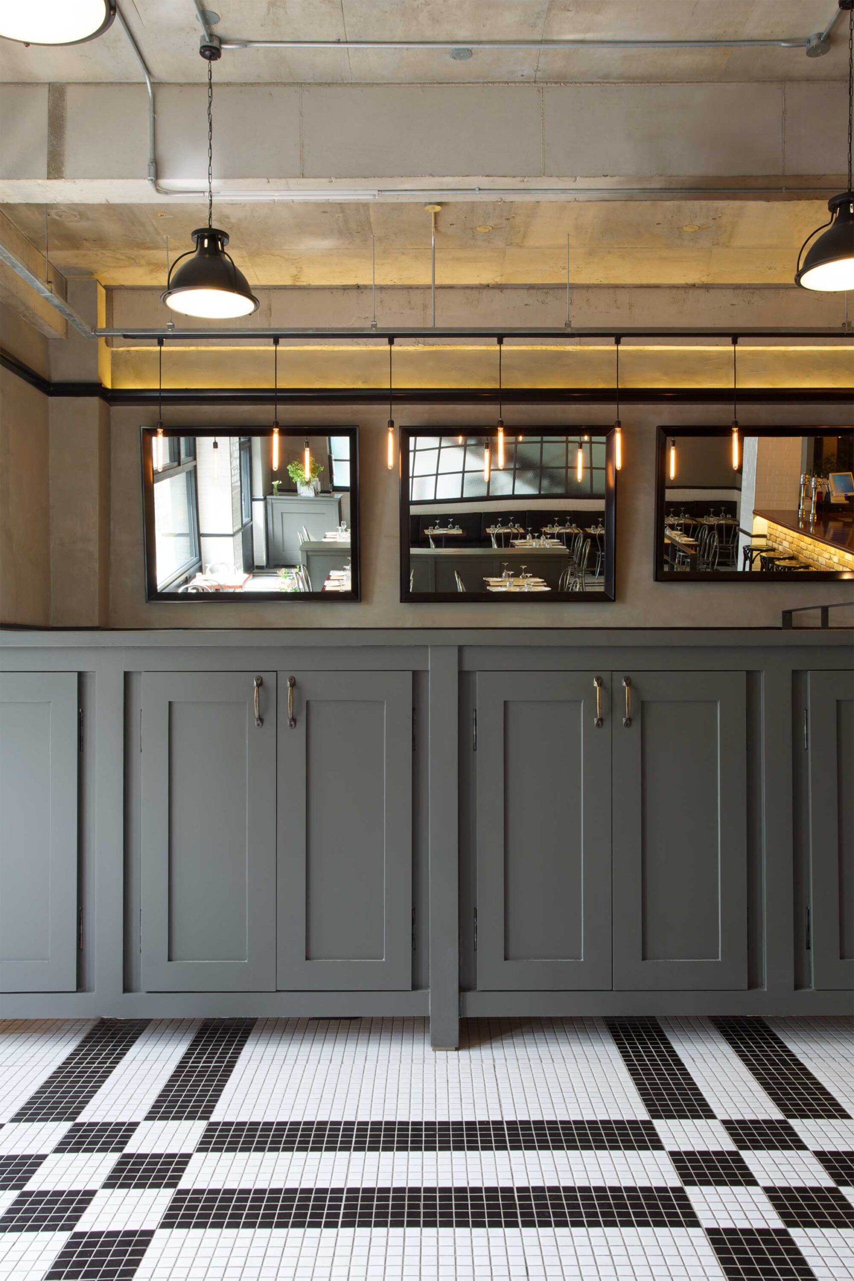 Grey counter in the center of Libertine bar and restaurant in Itaewon, Seoul, with a modern, minimalist design featuring white and black tiles and large mirrors to create depth.