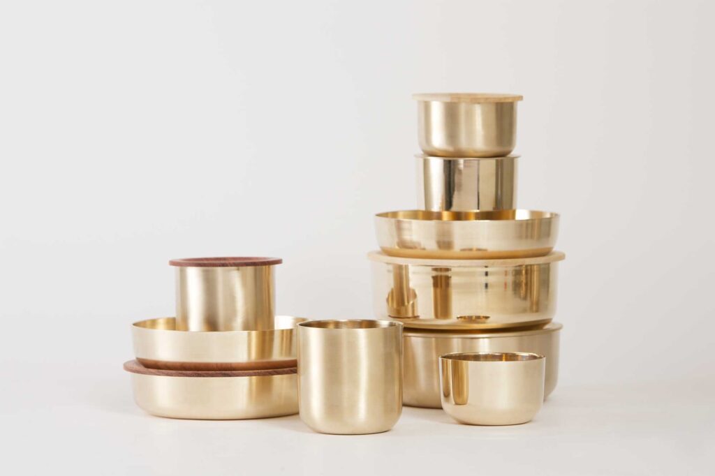 Cups and different sized bowls with lids for storing leftover food, part of the Korean traditional brass kitchenware collection designed by Gio Kisang and crafted by YÉOL Artisan of the Year, Kim Soo-Young, stacked on top of each other.