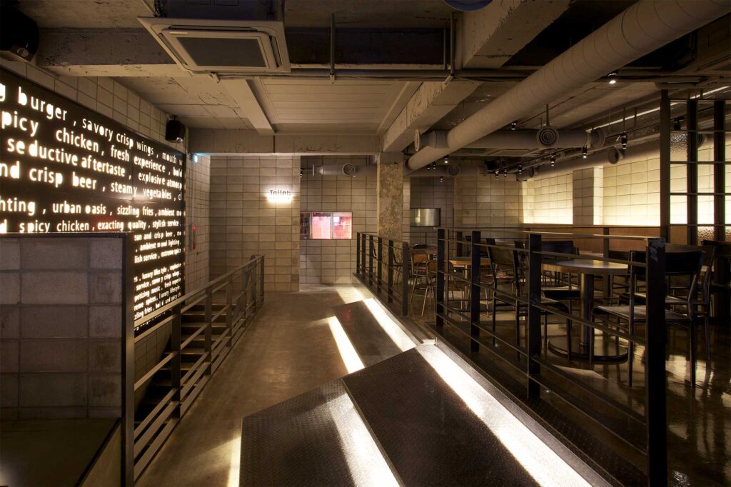Unique interior lighting concept for floor and wall with stenciled typography finish at Warehouse bar and restaurant in Seoul, featuring modern design with minimal decor using concrete and metal.