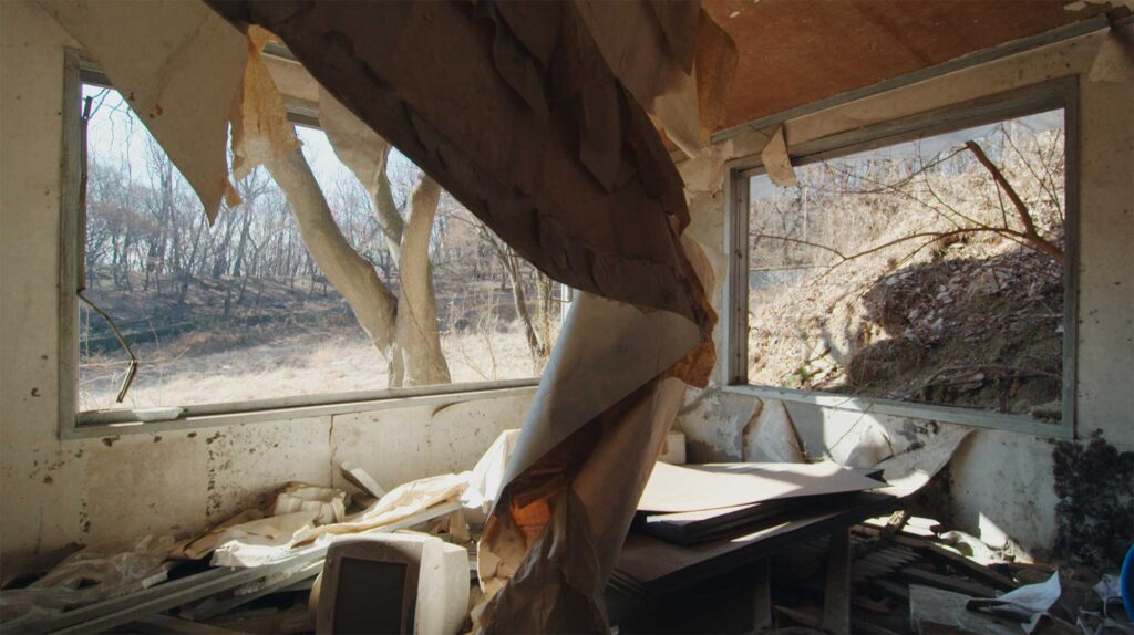 The living room of an abandoned building with wallpaper hanging from the ceiling and all window glass demolished, featured in the film Translating Furniture, showcasing Kwangho Lee's award-winning work.