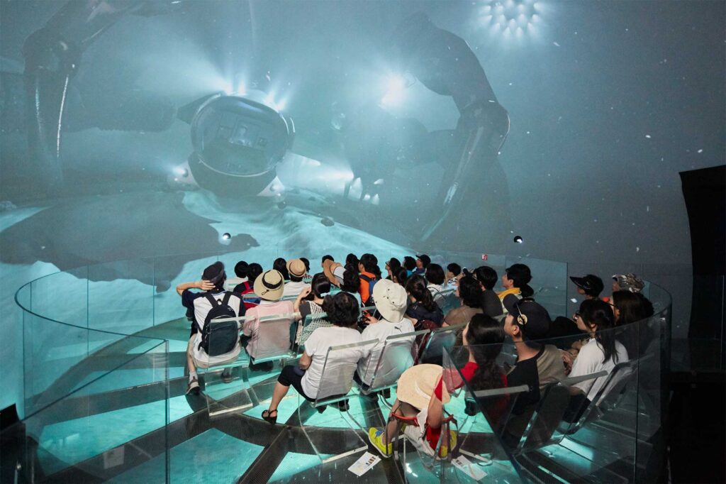 A group gathered for a video screening in a cubical theatre showcasing Germany's relationship to the ocean at the German Pavilion, World Exhibition, Yeosu, South Korea.