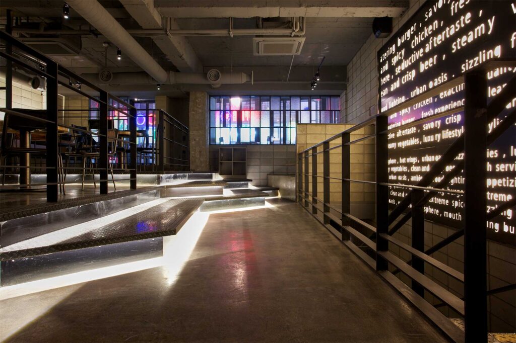 Unique interior lighting with stenciled typography at Warehouse bar and restaurant in Seoul, featuring modern decor with concrete and metal, enhanced by exterior neon lights.