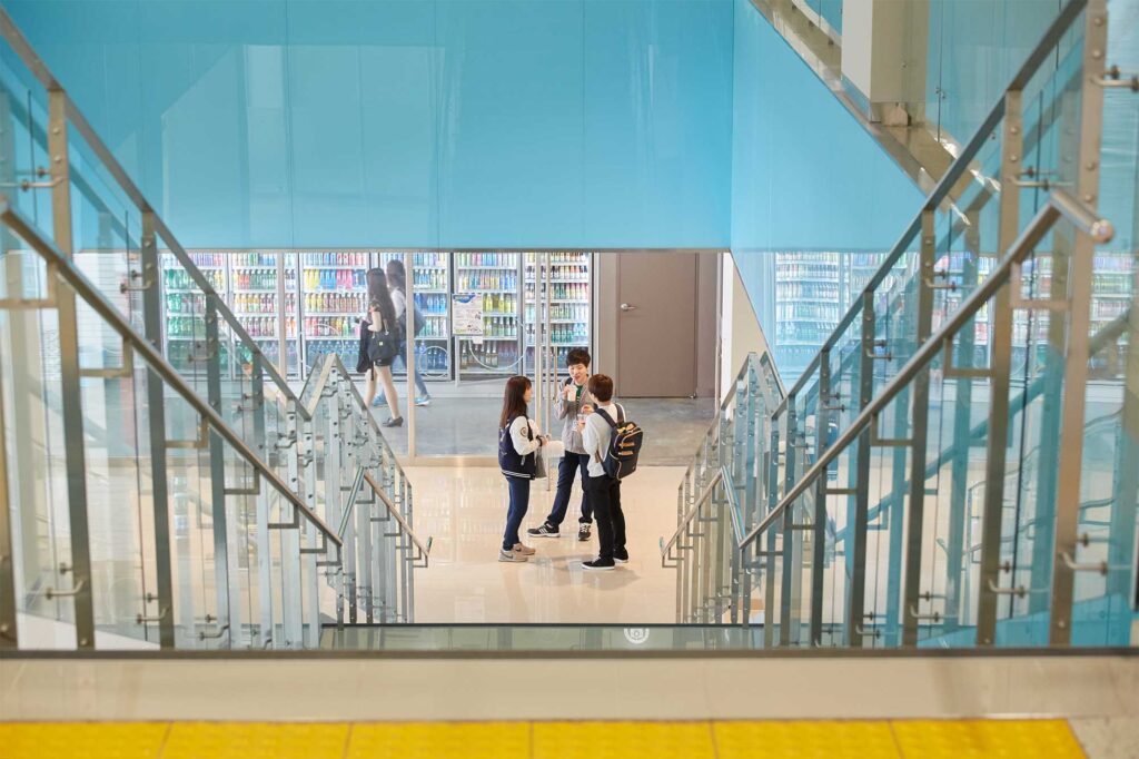 A small group of Underwood International College students gathers near an interior staircase by a campus convenience store at Yonsei University, Seoul, South Korea.