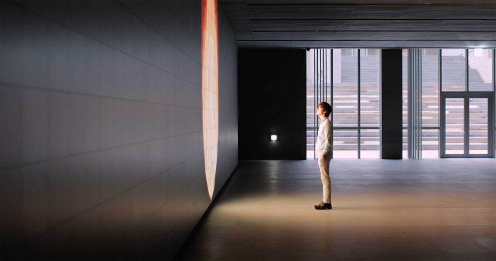 A man, illuminated by the screen's glow, stands before the Vision Hall Media Wall featuring Universal Everything's dynamic art installation at Hyundai Motor Group University, Mabuk Campus, South Korea.