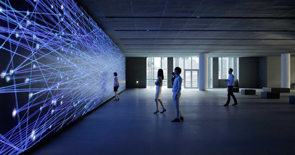 Visitors, bathed in blue light from the screen, gather around the Vision Hall Media Wall featuring Universal Everything's dynamic art installation at Hyundai Motor Group University, Mabuk Campus, South Korea.