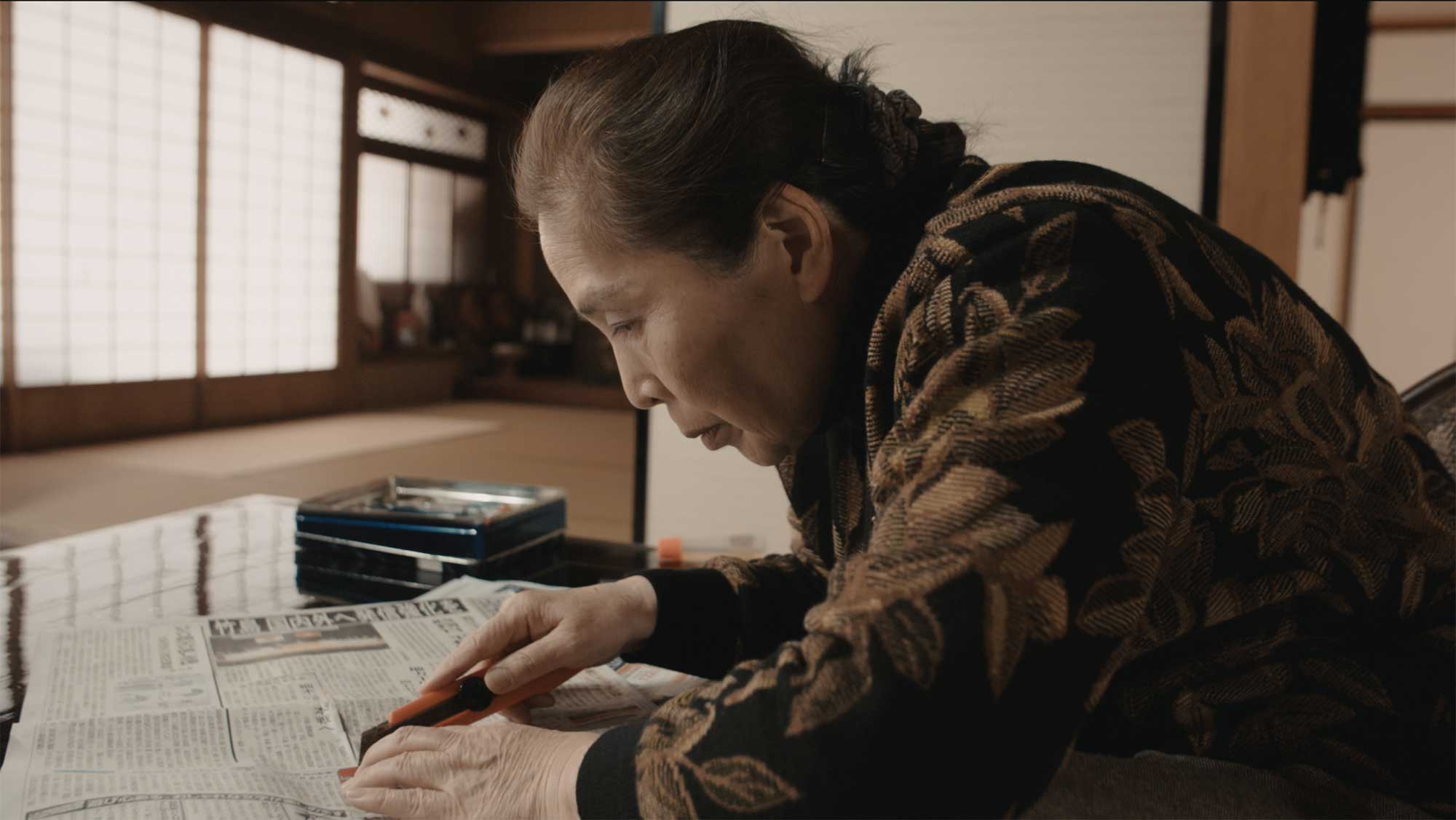 An elderly Japanese Takeshima activist cuts out newspaper articles at her home, focusing on the Dokdo Takeshima conflict for the film This Island is Ours.