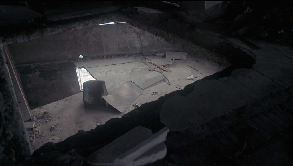 Looking down through ceiling cut-outs in an abandoned factory, an empty sofa sits in the middle, evoking memories of the past, from Nils Clauss's award-winning short film Bikini Words.