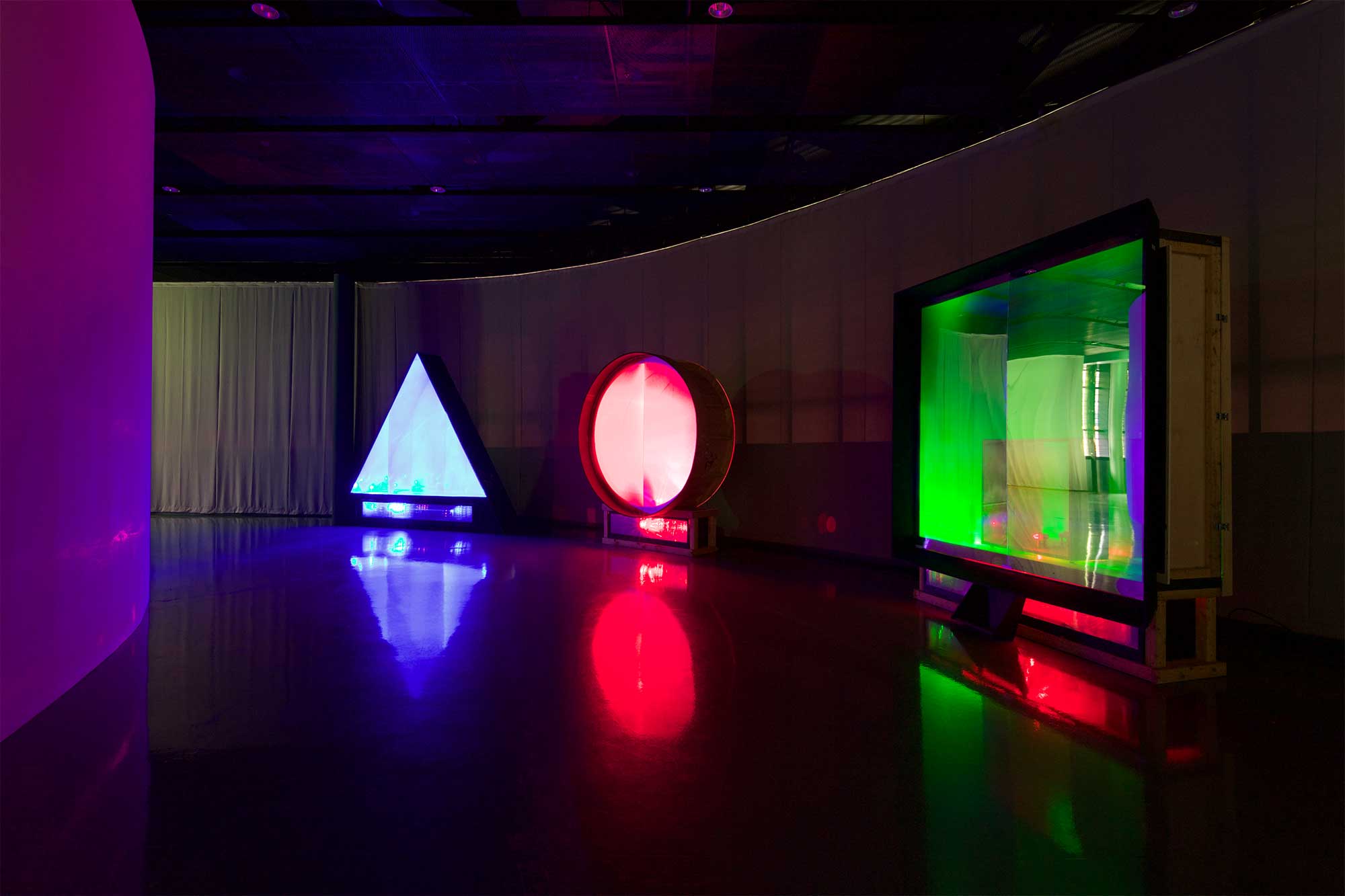 Three glowing installation pieces at INTERMEDIA THEATER exhibition, Nam June Paik Art Center, Seoul, South Korea, illuminate dark space, forming triangle, circle, and square.