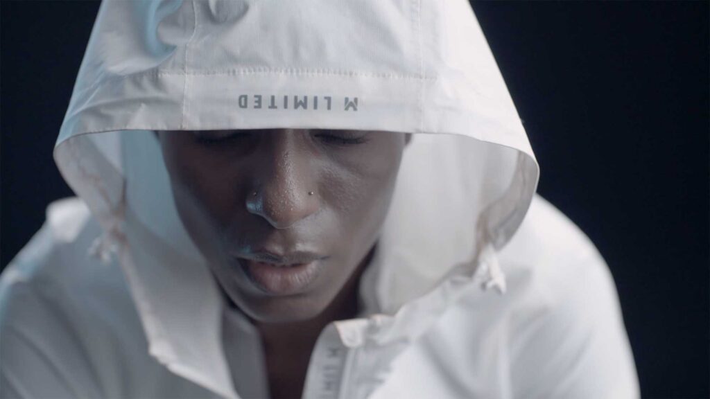 A woman of color, focused on her breathing, hides in silence under the hood of her white sports jacket for a Millet sports fashion campaign.