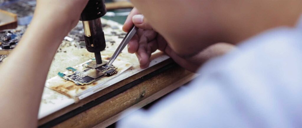 Inside a cell phone repair shop in Shenzhen, China, a technician is carefully brazing a chip on a phone in need of repair.