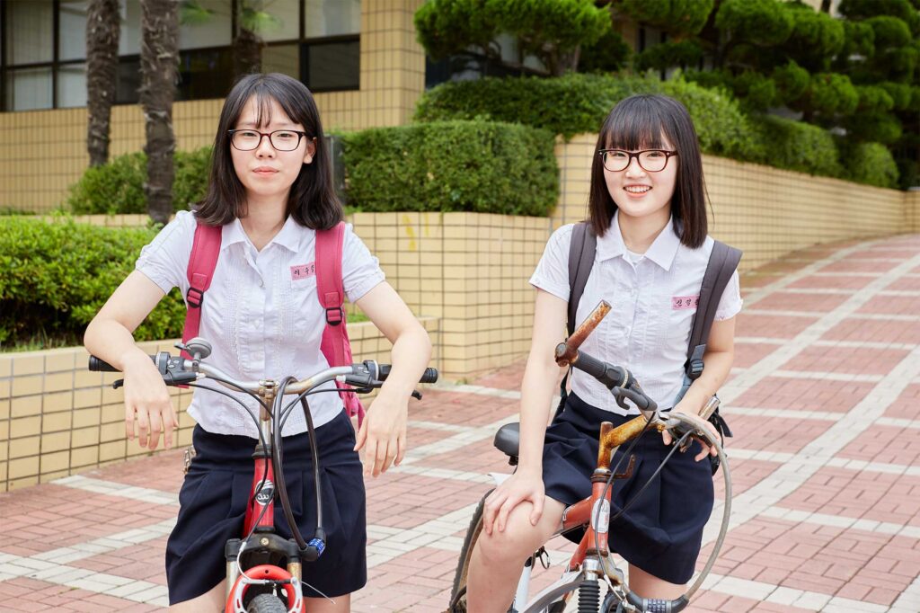 After school, two female students in school uniforms stand with their rusty bicycles outside Gwangyang Jecheol Middle & High School in Gwangyang, South Korea.