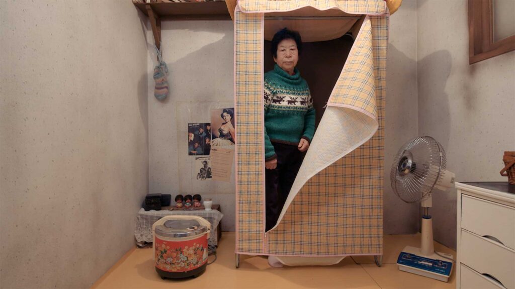 An elderly woman, a former factory worker during Korea's textile industry boom, stands in a so called Bikini closet within her cramped bee hive home, from Nils Clauss's award-winning short film Bikini Words.
