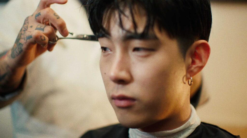 Korean rock musician gets haircut from barber with tattoos all over his hands in hip barber shop in Seoul, South Korea.