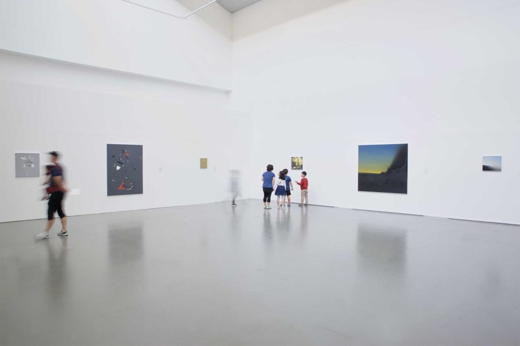 Larger-scale paintings displayed in white exhibition space with visitors, including children, admiring art, part of Irony & Idealism exhibition at Gyeonggi Museum of Modern Art, South Korea.