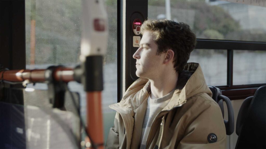 Minerva University student in Seoul, South Korea, sitting in city bus, looking outside as city flows by, exploring his new environment.