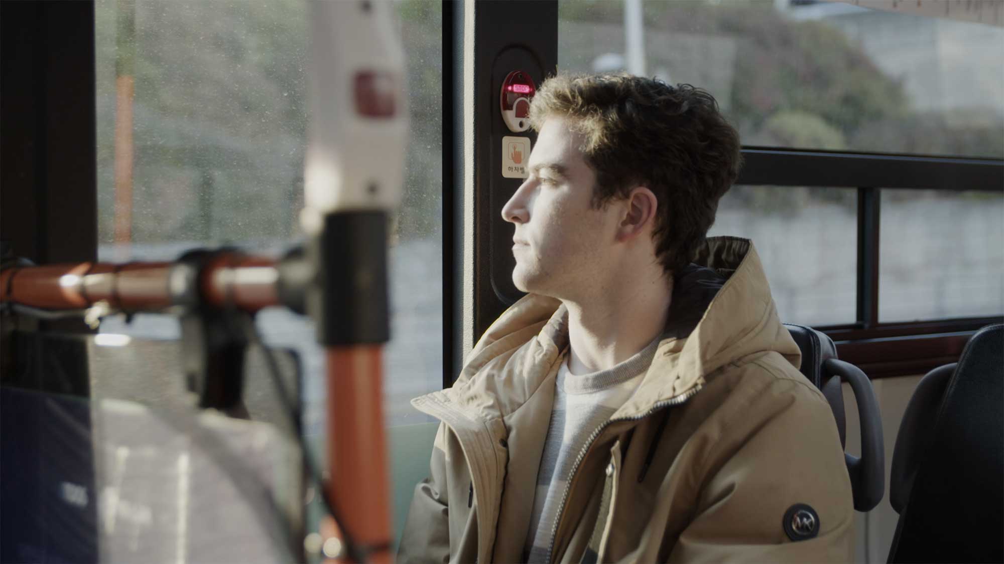 Minerva University student in Seoul, South Korea, sitting in city bus, looking outside as city flows by, exploring his new environment.