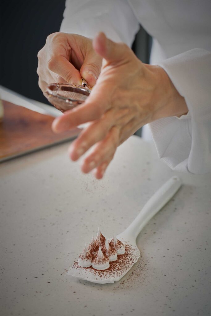 Pastry chef Eun Jeong Lee carefully adds cocoa powder to the elegantly shaped cream tips at EJ Baking in Seoul, captured for the ELLE & VIRE PROFESSIONNEL PRINT MAGAZINE series.