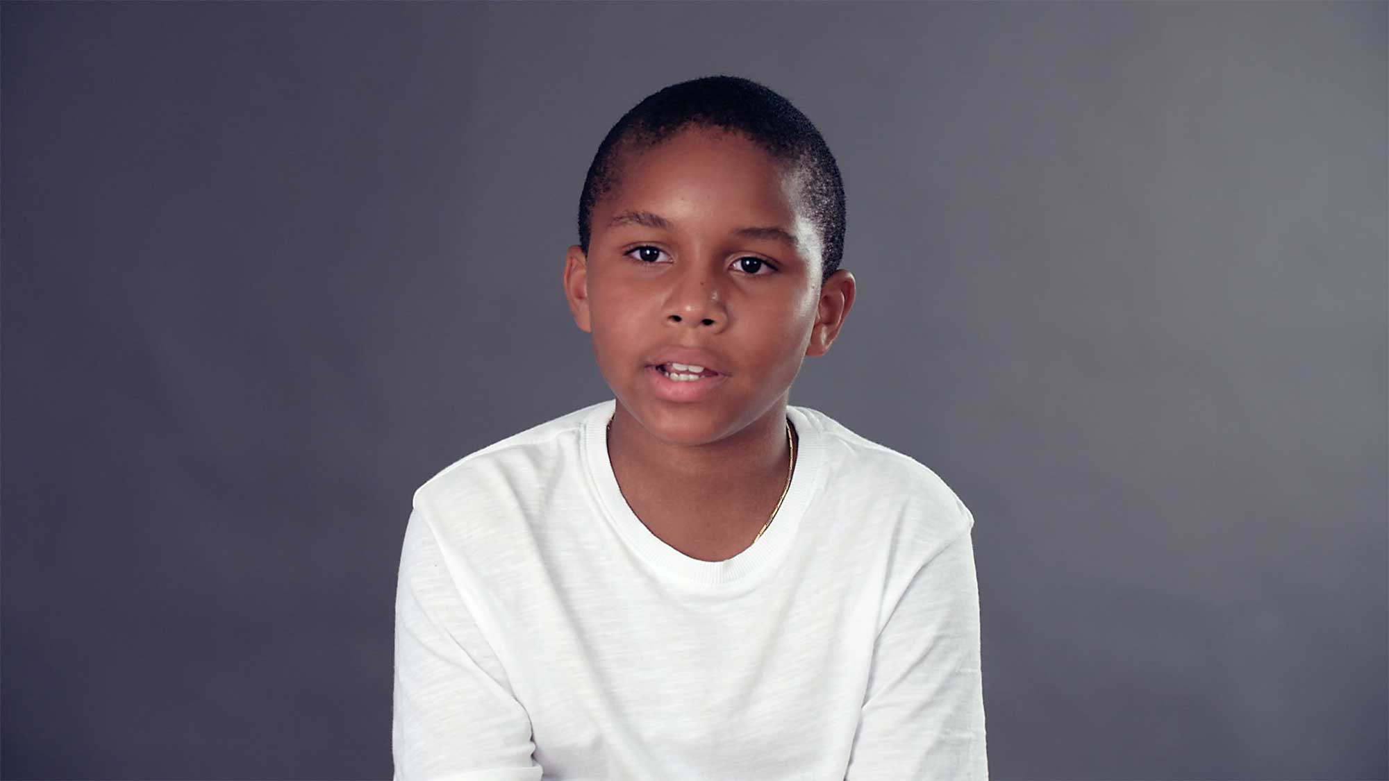 South American boy interviewed in front of grey colorama backdrop for short film IF, where children explore meaning of space and architecture.