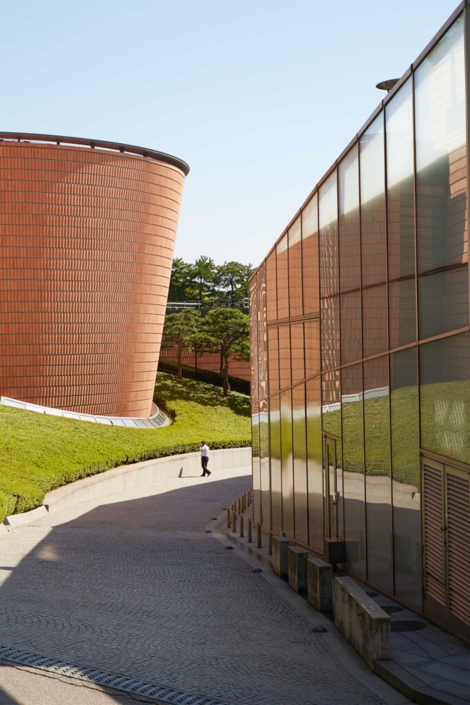 A man on the phone stands on the road dividing the Samsung Child Education & Culture Center, designed by Rem Koolhaas, and a terra cotta brick complex by Mario Botta, both part of Leeum, Samsung Museum of Art in Seoul, South Korea.