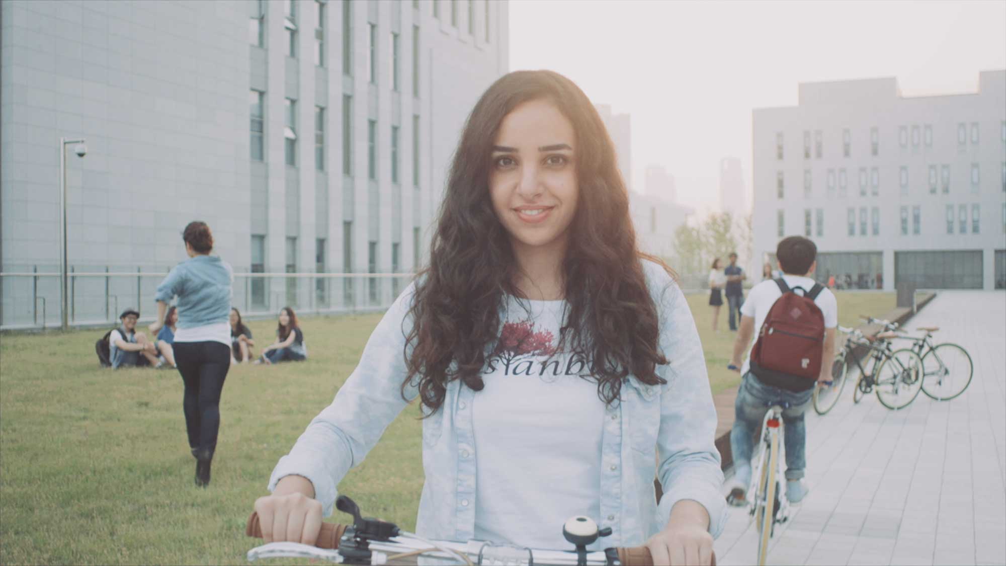 An Underwood International College student leaning on her bike beside a grassy patch at Yonsei University Songdo campus, enjoying time with friends after school.