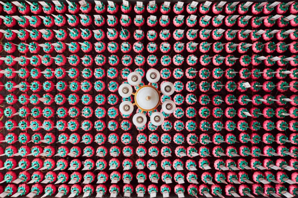 Ceiling of a Buddhist temple adorned with tightly organized rows of paper lotus flowers, with a chandelier centered in the middle, creating a serene atmosphere.