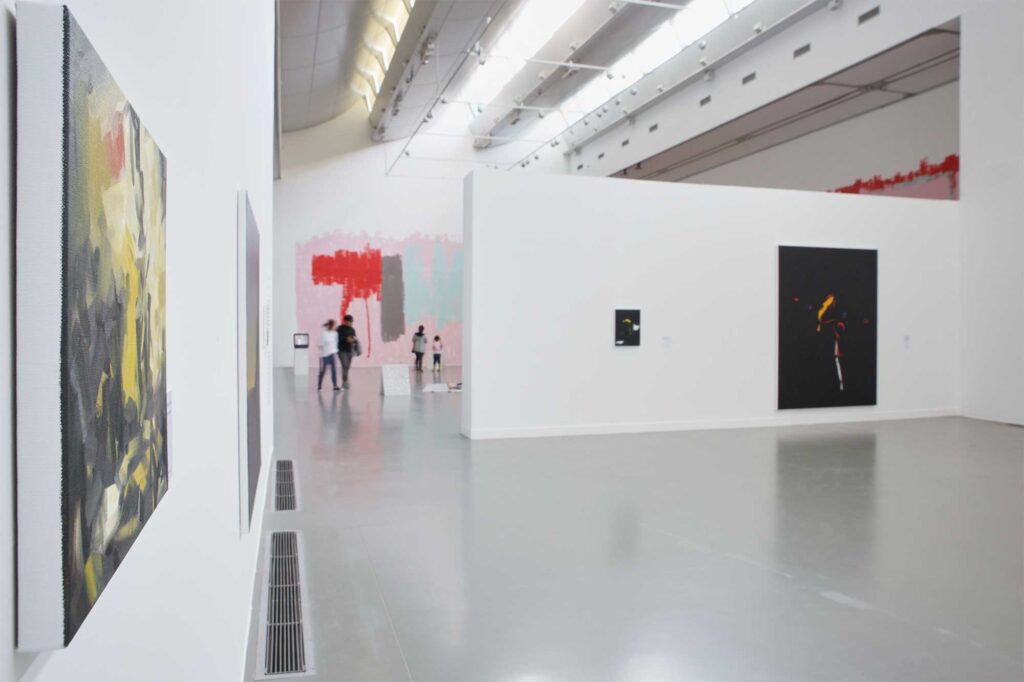 Larger-scale paintings displayed in white exhibition space with visitors walking past huge wall painting, part of Irony & Idealism exhibition at Gyeonggi Museum of Modern Art, South Korea.