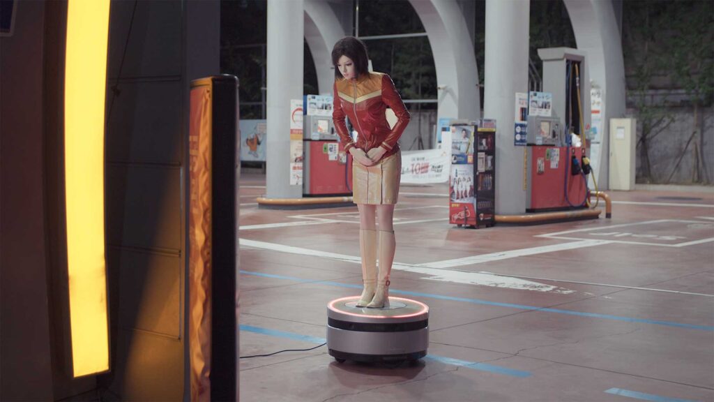 Plastic doll in short skirt shaped like human stands at filling station, bowing to customers in Seoul, South Korea.