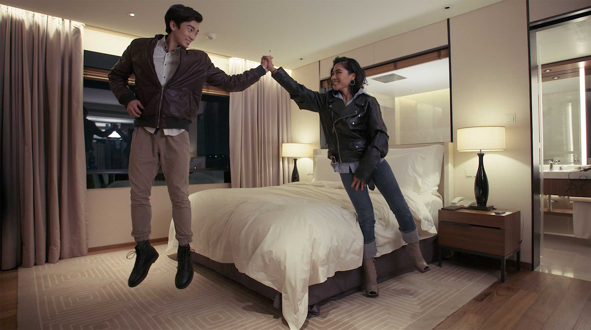 A young couple jumps into the air for a high-five, celebrating as they find a satisfying motel room in Seoul, South Korea.