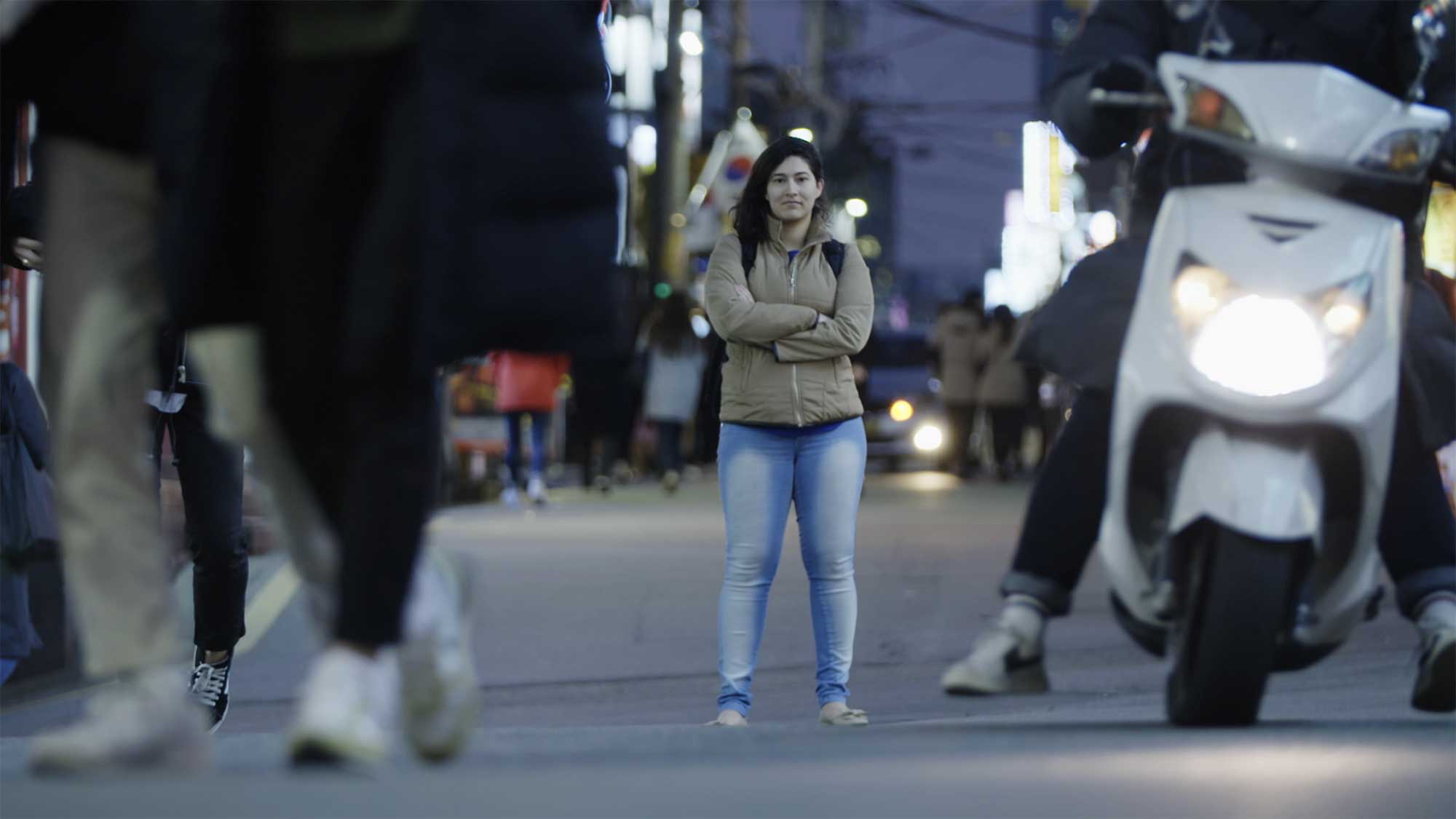 Minerva University student stands in middle of side road in Gangnam, Seoul, South Korea, as passerby and traffic flow past her.