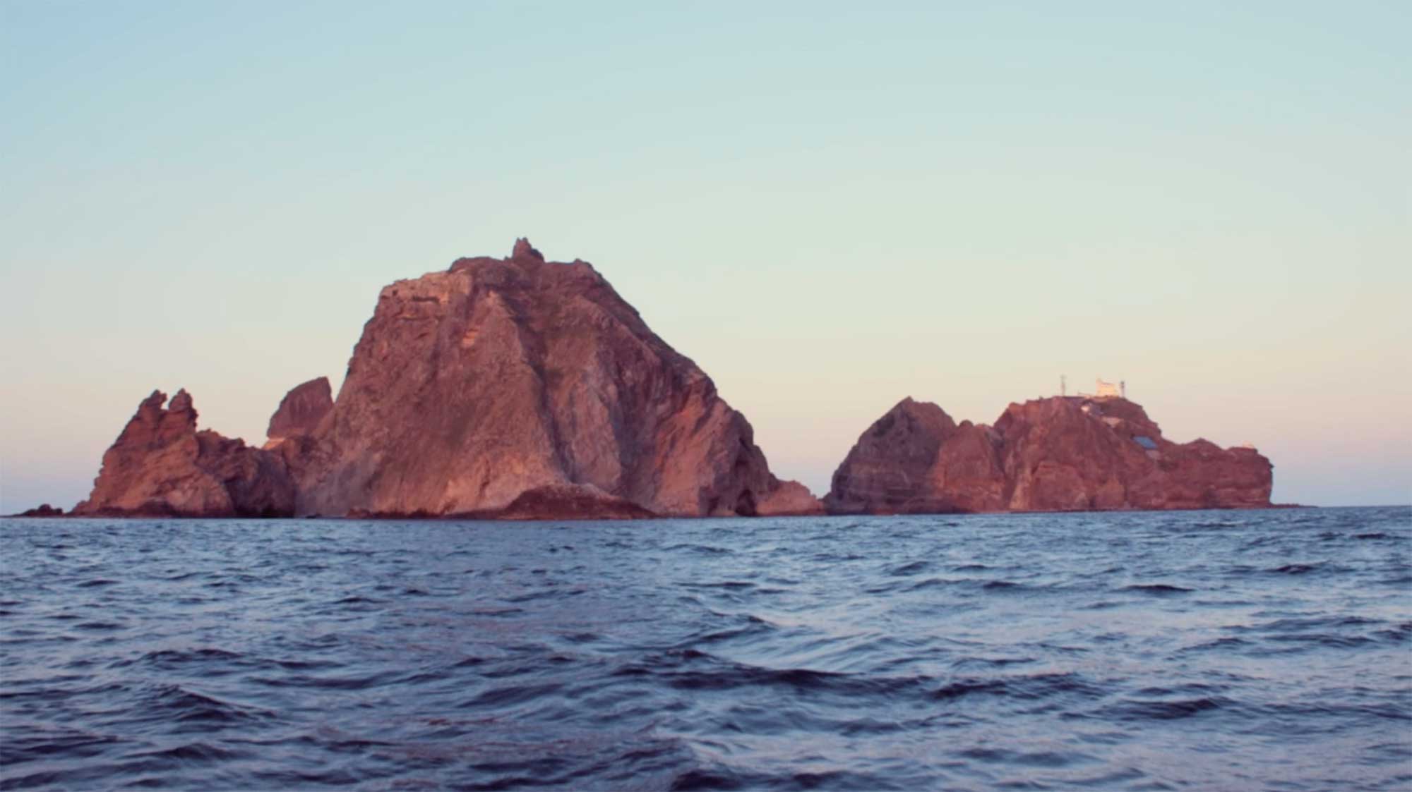 The island Dokdo Takeshima is seen from a distance at sunset in the film This Island is Ours, which explores activism related to the island dispute between Korea and Japan.