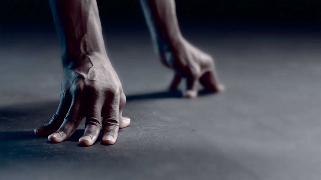 A woman of color is in a sprint starting pose, fingers pressed into the ground, showcasing determination and readiness for action in a Millet sports fashion campaign.