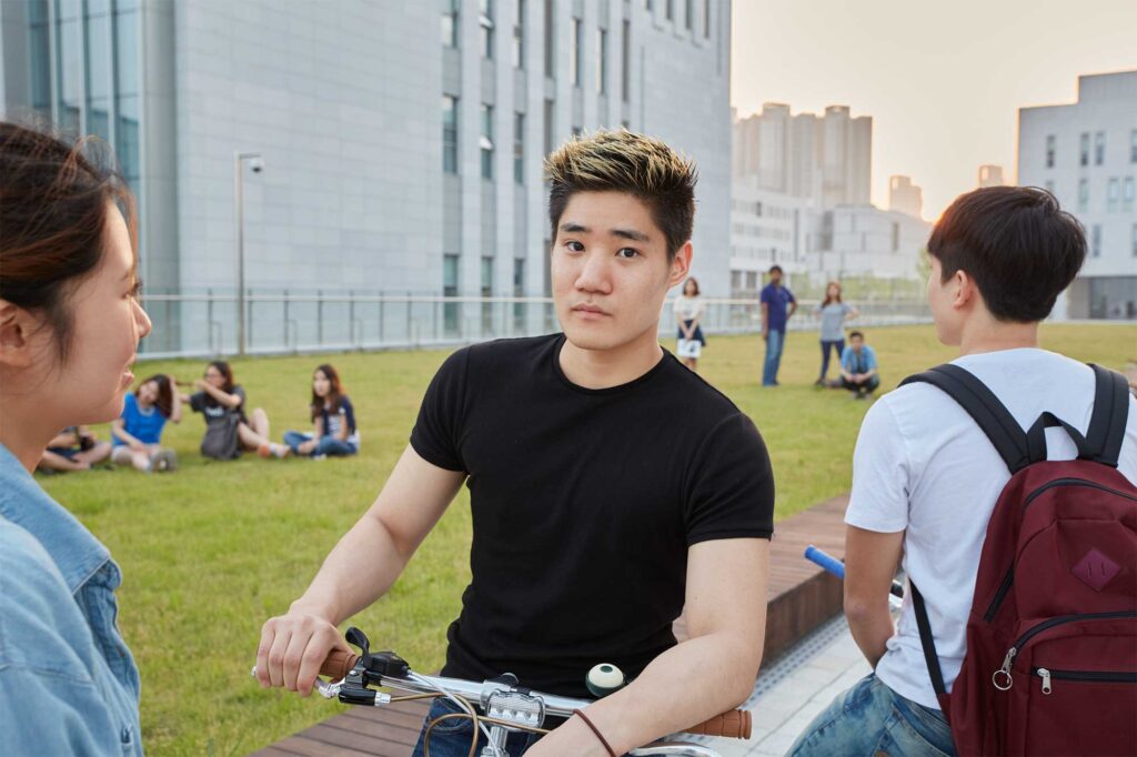 An Underwood International College student leaning on his bike next to a grassy patch at Yonsei University Songdo campus, hanging out with friends after school.