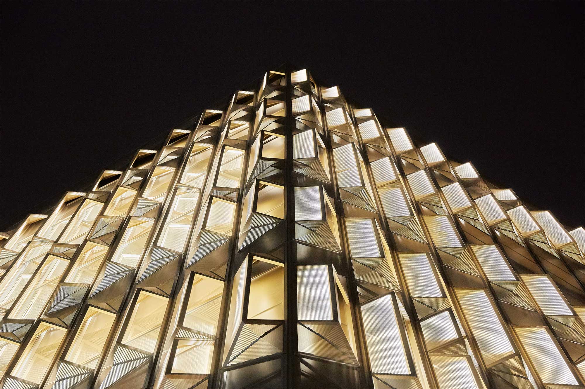 A semi-transparent wrapping of The Burberry Flagship Store in Seoul, South Korea, reveals its inner golden facade, enhancing its modern architecture and making it stand out against the black night sky.